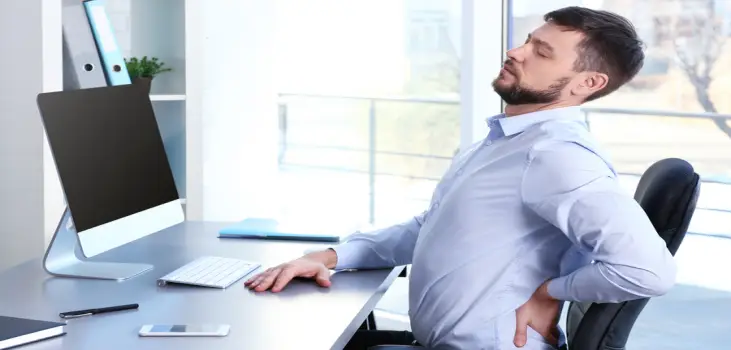 a young man working on his desk while holding his back